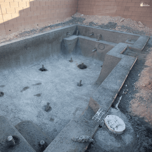 Pool remodel in progress with an empty concrete pool shell, exposed plumbing, unfinished surfaces, and surrounding construction materials.