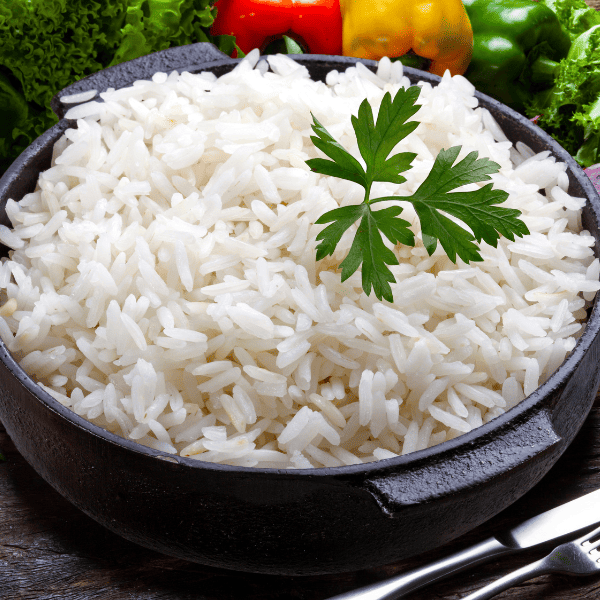 A bowl of fluffy white rice with parsley sits beside colorful peppers, ready to serve with Puerto Rican stews and other rice dishes.