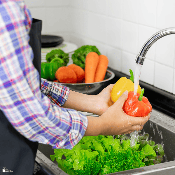 A person rinses bell peppers and leafy greens at the sink as part of a kitchen reset for easier meal prep.