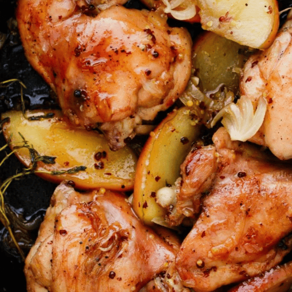 Apple Cider Chicken Thighs: Golden chicken thighs cook alongside apple wedges, onions, and herbs in a skillet.