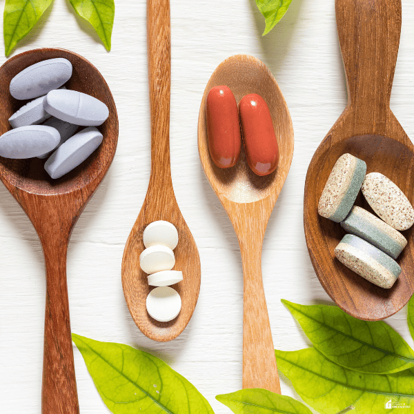 Assorted vitamins and supplements placed on wooden spoons with green leaves, representing common nutritional supplements families may consider adding to their routines.