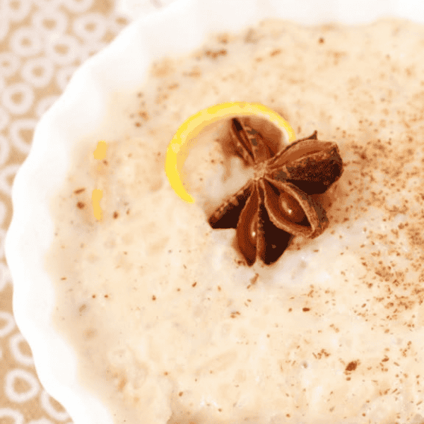 Arroz con Leche: Creamy rice pudding in a white bowl is dusted with cinnamon and topped with star anise and citrus peel.