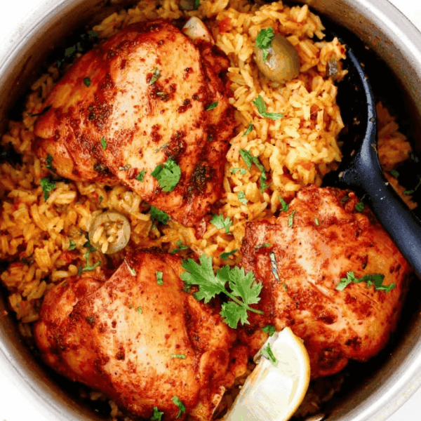 Arroz con Pollo: Golden chicken pieces rest on seasoned rice with green olives, fresh herbs, and a lime wedge in a cooking pot.