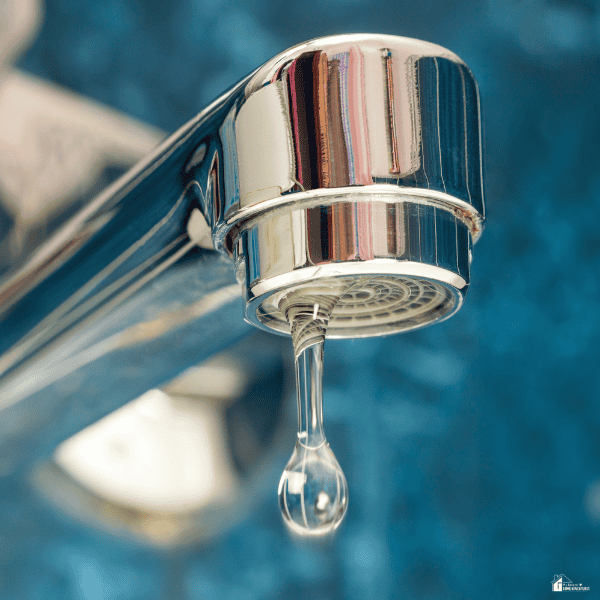 A drop hangs from a chrome faucet, showing a small leak that could signal a household plumbing problem.