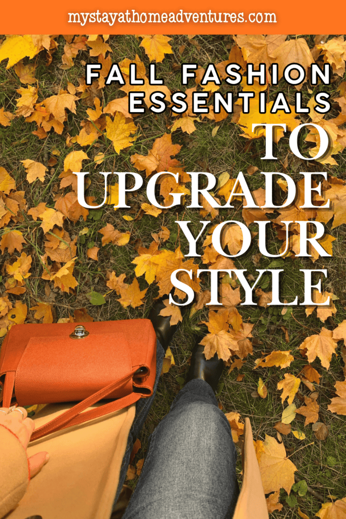 An orange handbag, tan coat, jeans, and black boots create a fall outfit among scattered yellow leaves.