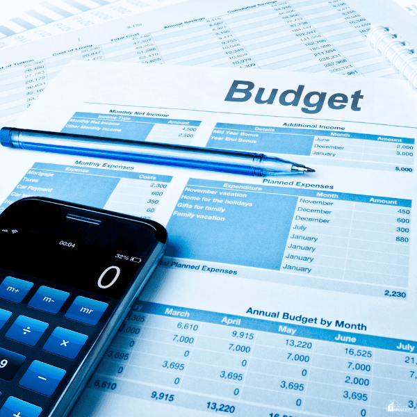 A phone displaying a calculator rests on printed financial worksheets, illustrating how a budgeting app can help track income and expenses.