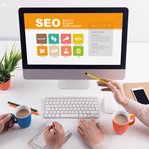 A team reviews an SEO dashboard on a desktop monitor while taking notes and discussing the work.