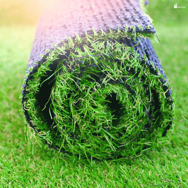 A roll of artificial lawn shows green fibers and dark backing before installation.