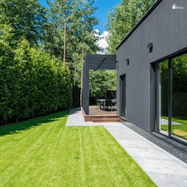 Artificial lawn covers a yard beside a modern home, bordered by a stone path and wooden patio.