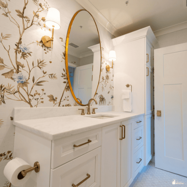 Blue and cream flower prints cover the bathroom wall behind a white vanity and oval mirror.