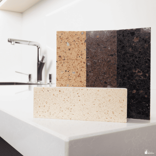 Four countertop samples in beige, brown, and black sit beside a sink for choosing kitchen remodel materials.
