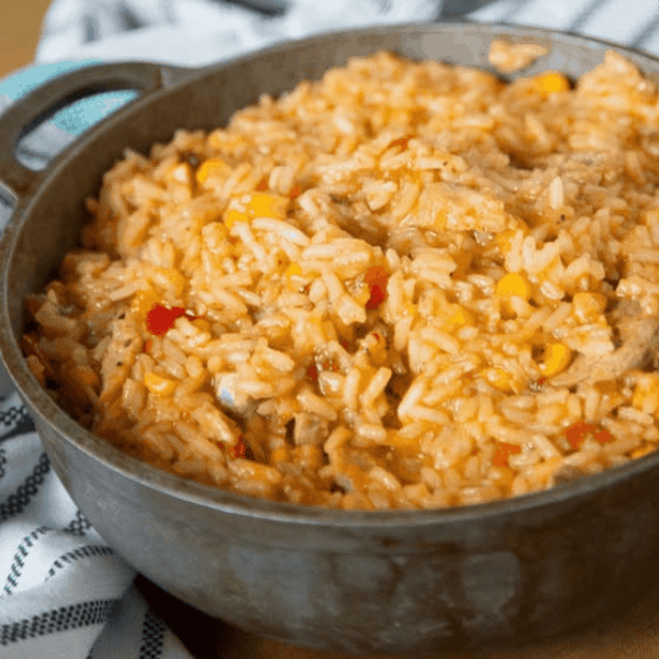Instant Pot Arroz con Chuletas: A dark cooking pot holds seasoned rice mixed with pork pieces and diced peppers.
