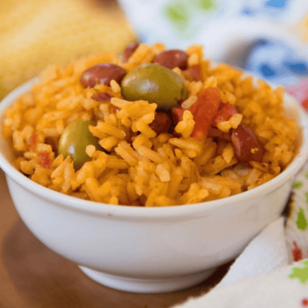 Instant Pot Arroz con Habichuelas: A white bowl holds golden rice with red beans, green olives, and diced vegetables.