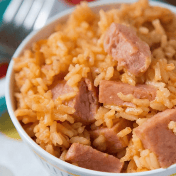 Instant Pot Arroz con Jamonilla: A close-up of a white bowl shows orange seasoned rice mixed with chunks of Spam.