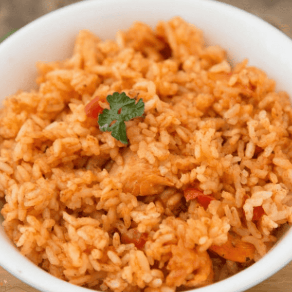 Instant Pot Chicken and Rice: A white bowl holds orange seasoned rice with chicken pieces and a small herb garnish.