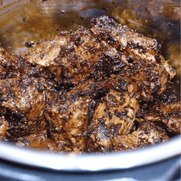 Instant Pot Puerto Rican Beef Barbacoa: A browned, spice-coated beef roast sits in savory cooking juices inside a pressure cooker.