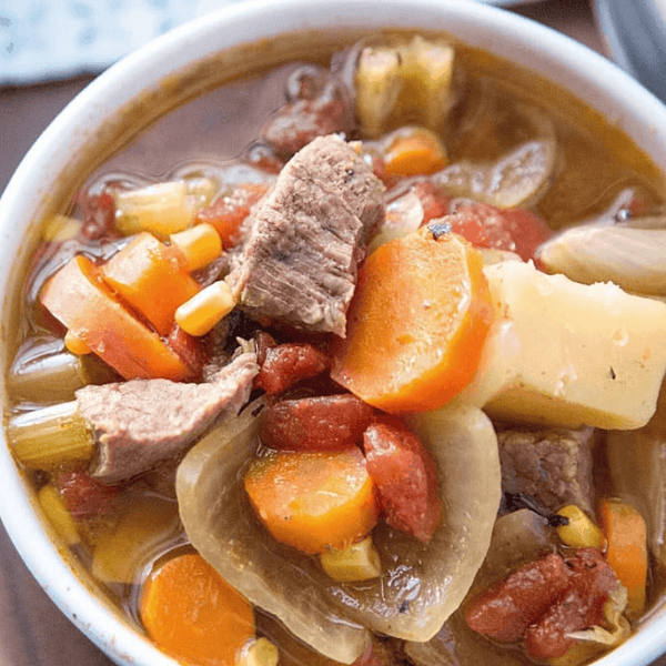 Instant Pot Sopa de Carne: A white bowl holds beef soup with carrots, potatoes, onion, celery, corn, and tomatoes.