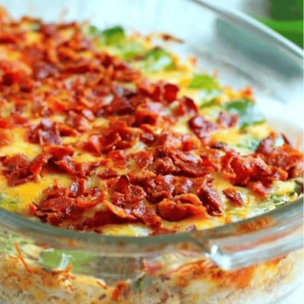 Keto Jalapeño Popper Chicken Casserole: A glass baking dish holds a cheesy chicken casserole topped with chopped bacon and green jalapeño pieces.