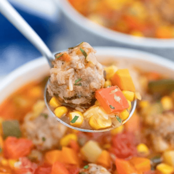 Mexican Meatball Soup: A spoon lifts a meatball and colorful vegetables above a bowl of tomato-based soup.