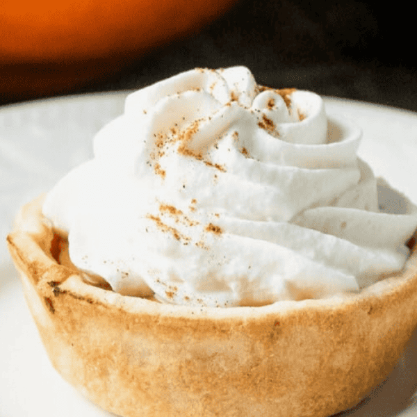 Mini Pumpkin Pies: A small pumpkin pie in a golden pastry crust is topped with a generous swirl of whipped cream and a dusting of spice.