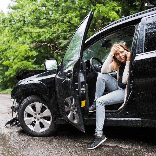 A distressed traveler sits inside a badly damaged rental car after an accident on a wooded road.