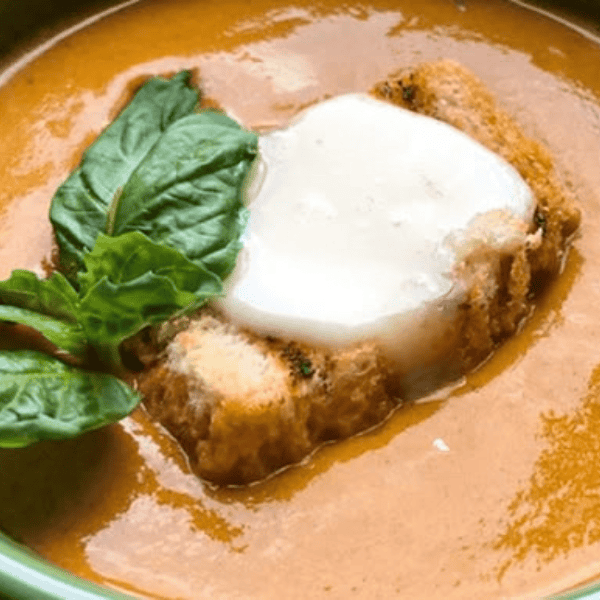 Roasted Yellow Tomato Soup with Grilled Cheese Croutons: Smooth golden tomato soup is topped with toasted bread, melted cheese, and fresh basil leaves.
