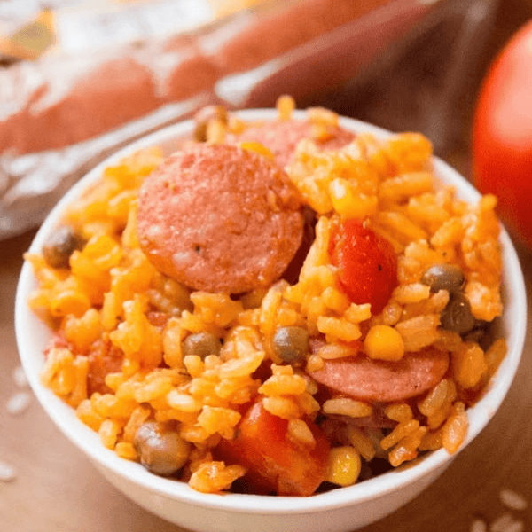 Sausage with Puerto Rican Rice with Pigeon Peas: A white bowl holds golden rice mixed with smoked sausage slices, pigeon peas, corn, and diced tomatoes.