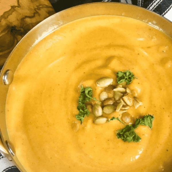 Slow Cooker Curried Butternut Squash Soup: Creamy orange butternut squash soup fills a metal bowl garnished with pumpkin seeds and chopped herbs.