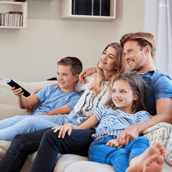 A family sits together on a couch with a remote control, illustrating family viewing choices informed by TV ratings.