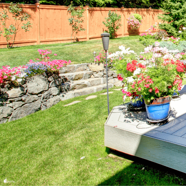 A wooden privacy fence upgrades a landscaped family garden with added seclusion around the lawn, flower beds, and deck.