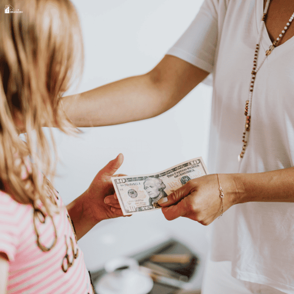 An adult hands a banknote to a child, illustrating how children can learn money management through everyday choices.