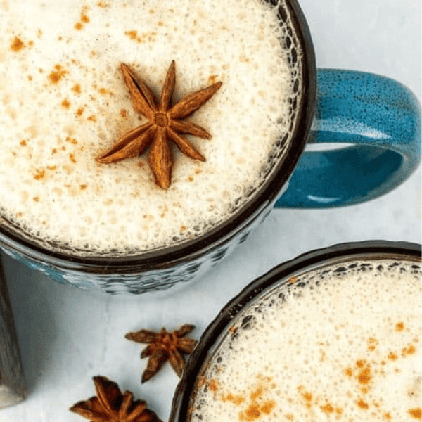 Vanilla Chai Latte: Two mugs of frothy chai are dusted with cinnamon, with a star anise garnish on one mug.