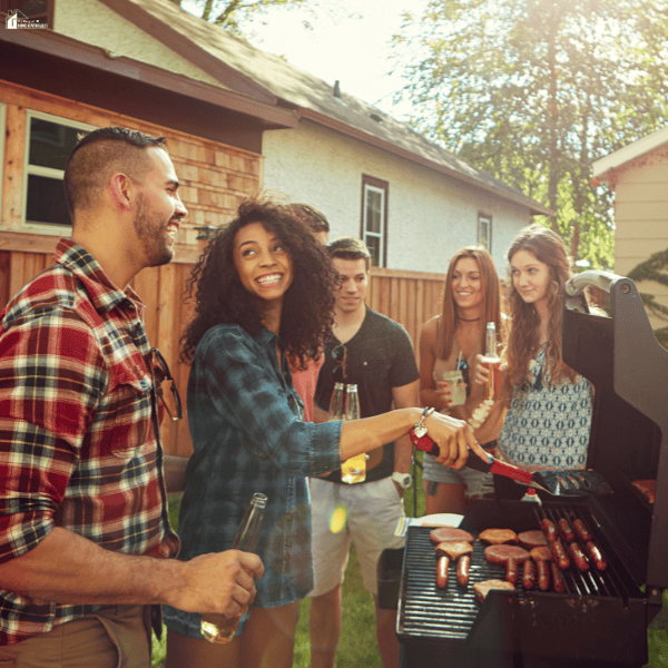 Friends gather around a grill for backyard entertaining while one person cooks burgers and sausages.