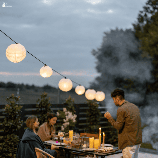 Glowing lanterns light an outdoor dinner table set up for backyard entertaining at dusk.