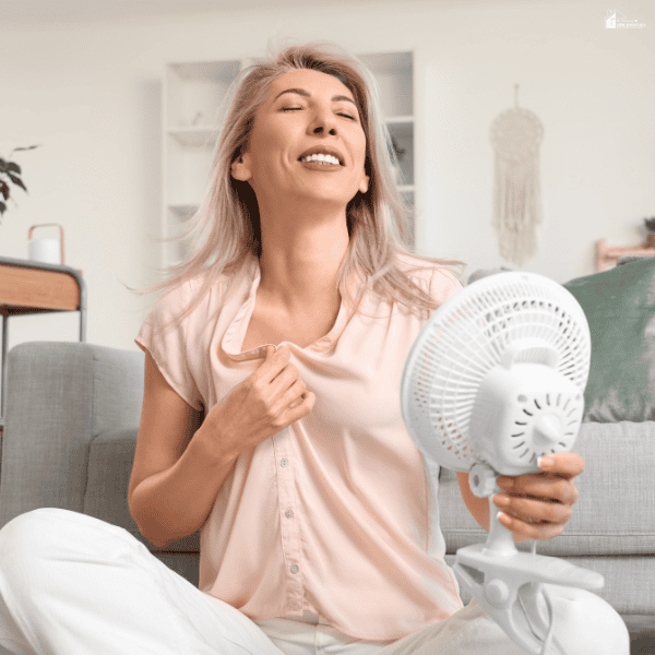 A woman cools herself with a small fan in a bright room where she may want to reduce heat and glare.