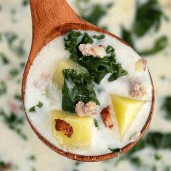 Zuppa Toscana: A wooden ladle holds creamy soup with potato chunks, sausage pieces, and leafy kale.