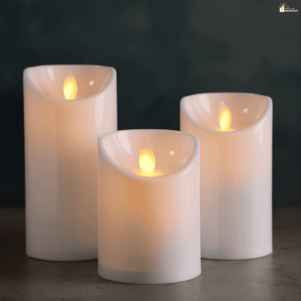 Three white flameless pillar candles with glowing flame-shaped lights stand on a gray surface against a dark background.