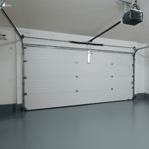 A closed white sectional door and ceiling-mounted opener sit above a smooth concrete garage floor.