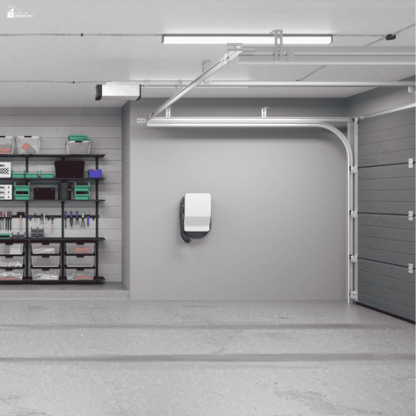 A tidy garage features a concrete floor, organised tool shelves, storage bins, and a wall-mounted charging unit.