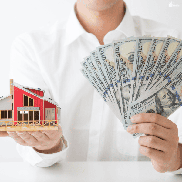 Person holding a red model house and a fan of hundred-dollar bills, representing cash home buyers purchasing residential properties.