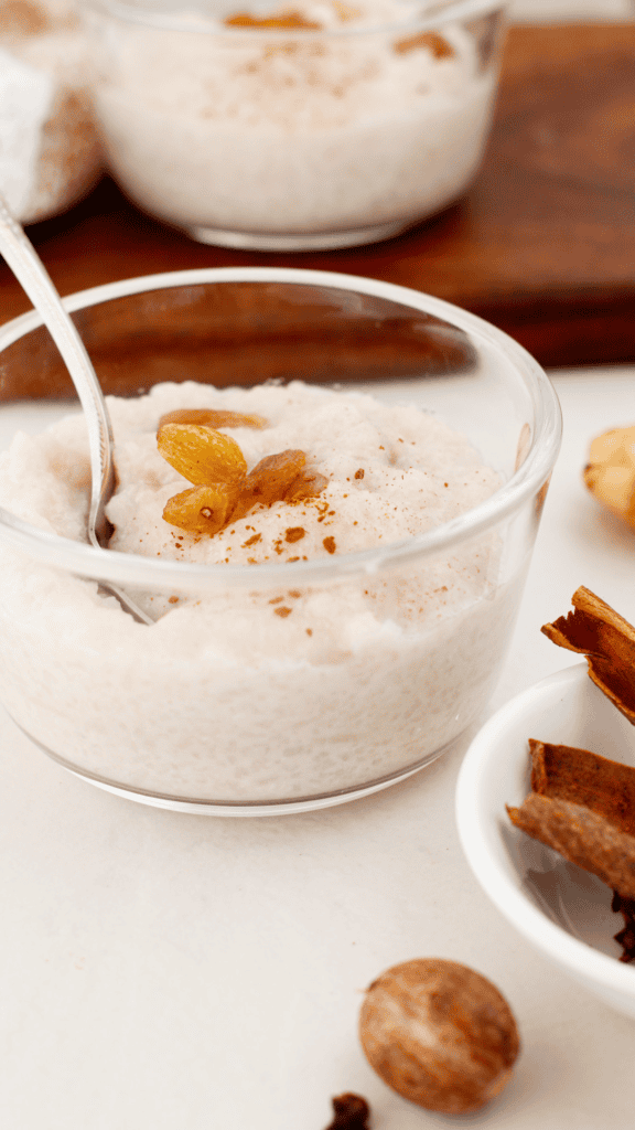 Creamy Arroz Dulce coconut rice pudding topped with golden raisins and ground cinnamon in a glass bowl with a silver spoon.