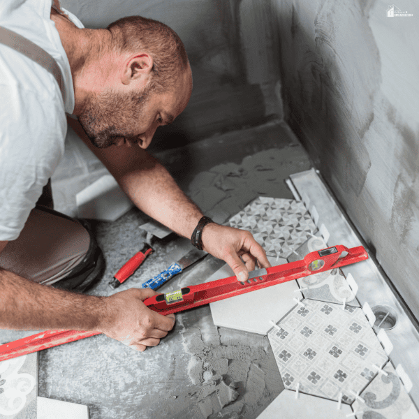 A man checks hexagonal floor tiles with a red spirit level during bathroom remodeling.