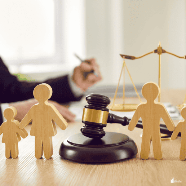 Wooden parent and child figures surround a gavel and balance scales, symbolizing family laws and child custody proceedings.