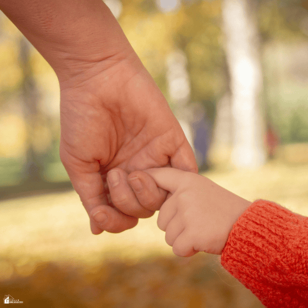 A child holds an adult’s finger outdoors, representing parental care in the context of family laws and child custody.