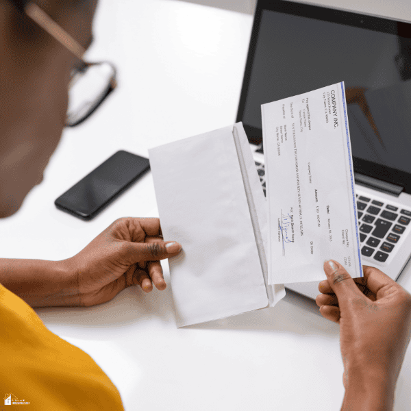 A person holds a check and envelope beside a laptop, illustrating income planning related to early paycheck access.
