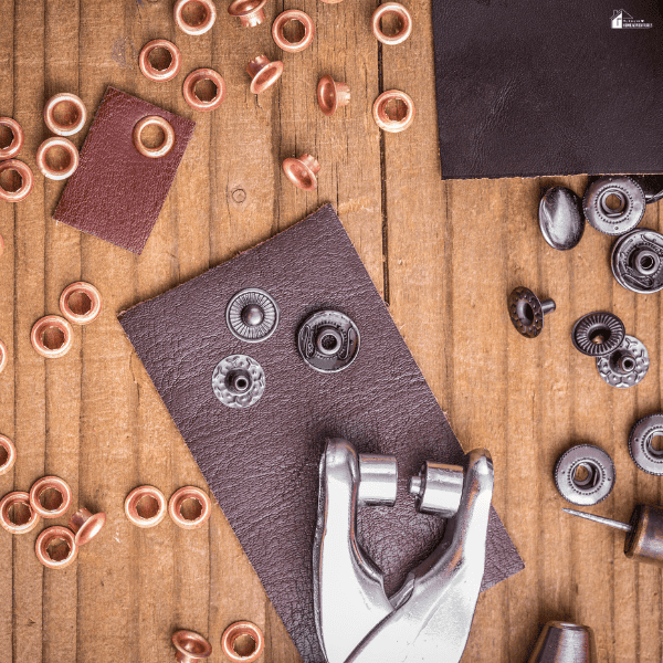 Eyelets, snap fasteners, and setting pliers lie on a wooden workbench for finishing a hole in leather.