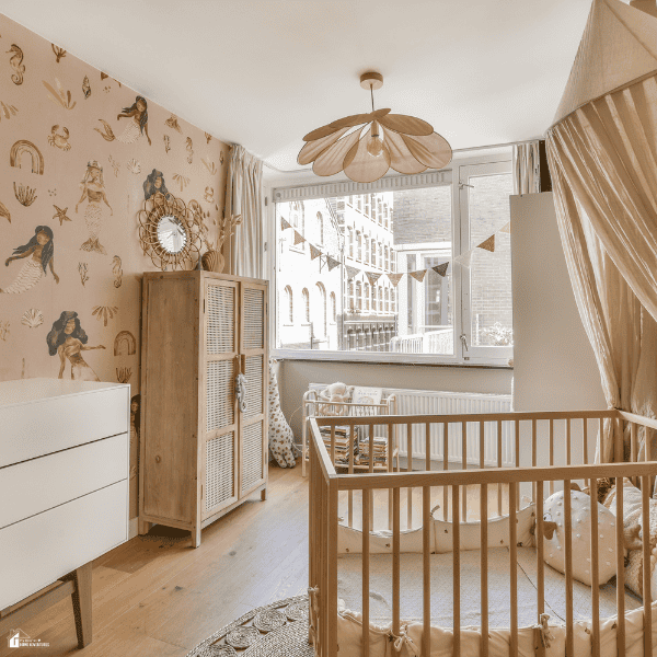 Mermaid baby wallpaper pairs with a wooden crib, beige canopy, and woven cabinet in a bright nursery.