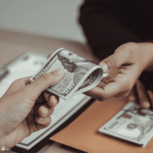 Hands exchange banknotes over a desk with paperwork, illustrating fees to consider when comparing an RPL training provider.
