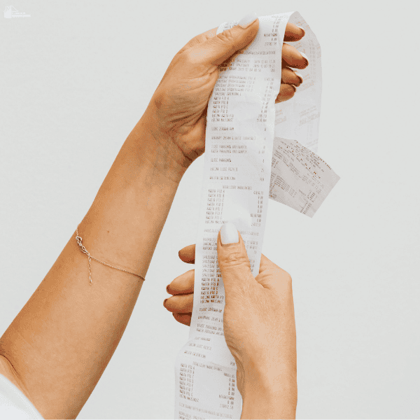 Hands hold a long receipt to review food purchases and track a grocery budget.