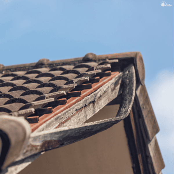 Peeling fascia paint and a sagging gutter beneath curved tiles show exterior deterioration associated with roof decay.